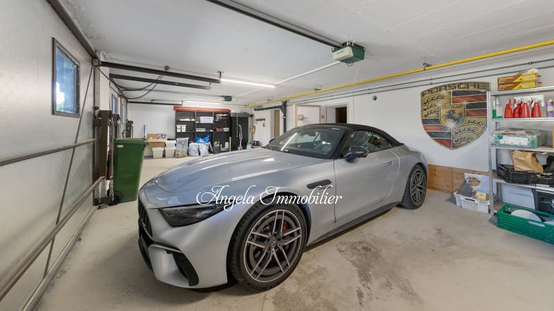 The image shows a garage with a silver Porsche sports car parked inside. The garage has various storage items and equipment visible, as well as Porsche-related decor on the walls.