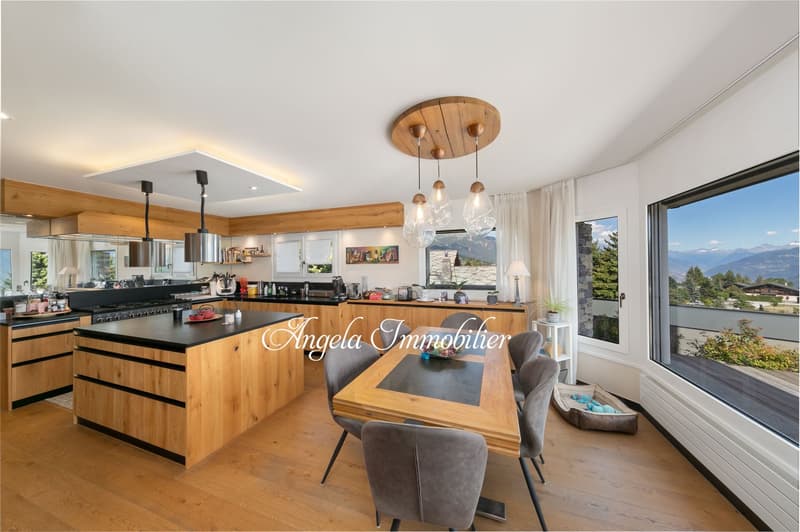 Open-concept kitchen and dining area with wooden beams, large windows providing a scenic view, modern kitchen with black countertops and wooden cabinetry, pendant lighting fixtures, and a dining table with grey upholstered chairs.