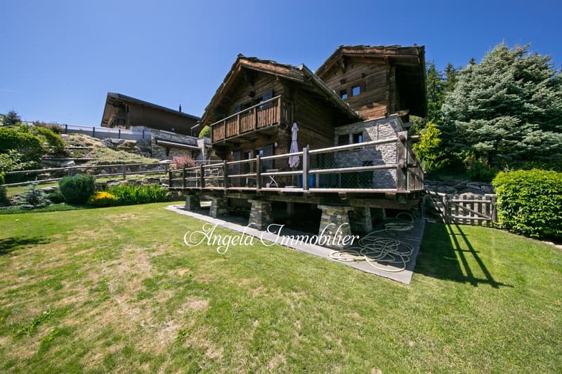 Two-story wooden chalet-style house with stone accents, balconies, and a well-maintained garden with a grassy lawn