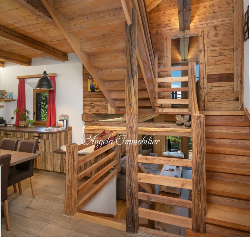 Rustic wooden interior with exposed beams, wooden staircase, fireplace, dining area, and shelving with decor