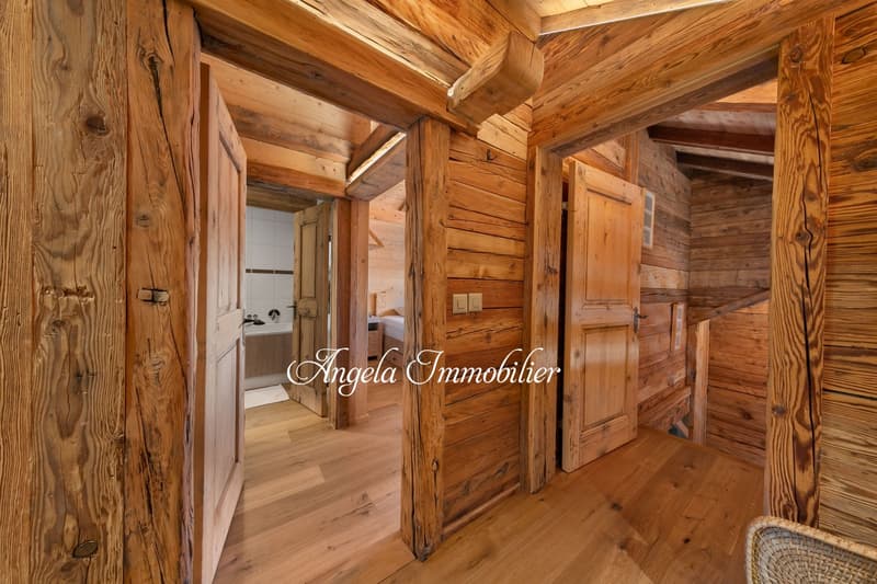 Rustic wooden cabin interior with exposed wooden beams and walls, wooden flooring, and a doorway leading to a bathroom or other room.