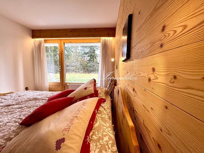 large bed, wooden walls, large windows, red pillows, white blankets, wooden bedhead, radiator, wall lamp