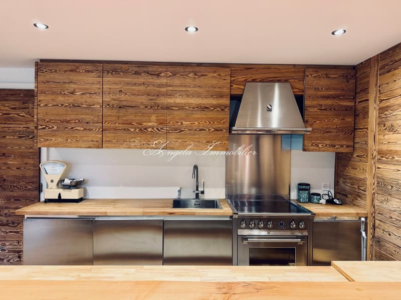 Modern open kitchen with wooden cabinets, stainless steel appliances, wooden countertop, wooden walls, integrated dishwasher and washing machine