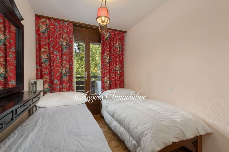 Two beds, red curtains, white bedding, radiator, chandelier, wooden floor, window with balcony