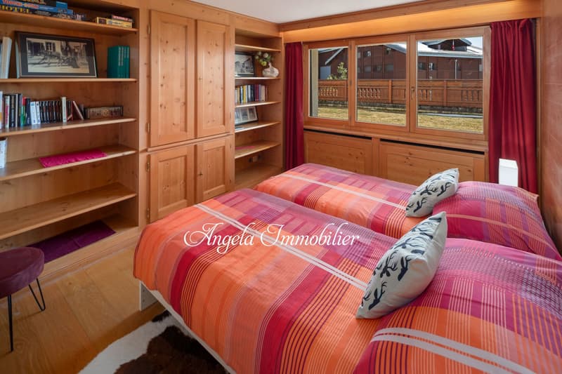 bedroom with wooden bed, pillows, wardrobe, shelves with books and photos, carpet, red curtains