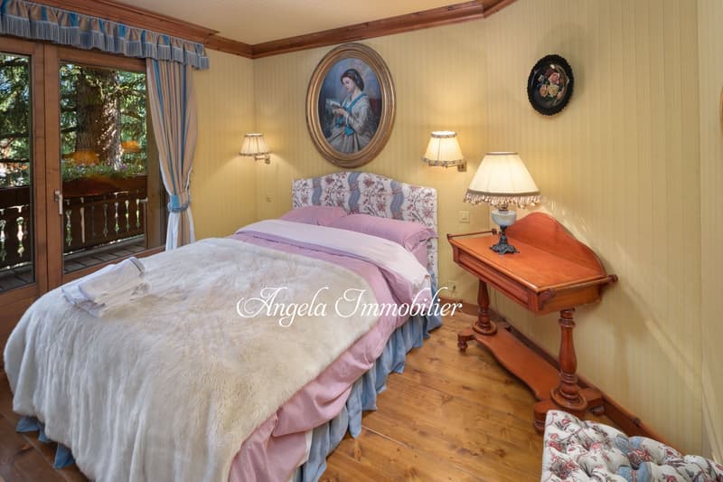 Cozy bedroom with wooden floors, yellow walls, large windows overlooking a balcony, a floral upholstered bed, wooden nightstand, and decorative wall art