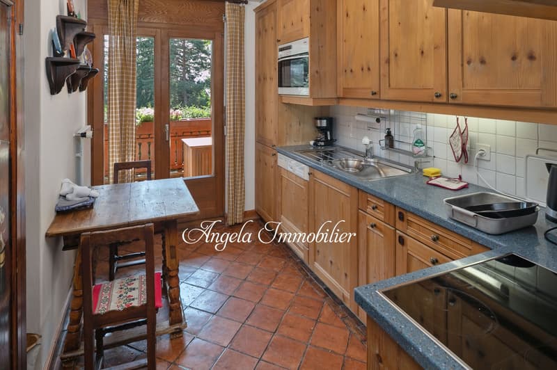 Rustic kitchen with wooden cabinets, tile flooring, large windows overlooking a balcony or terrace, and a dining table