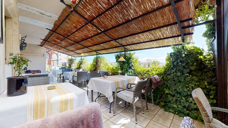 covered terrace with woven ceiling, tables and chairs with white cloths, tableware, outdoor plants