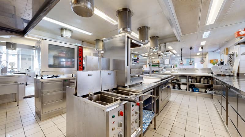 Commercial kitchen with modern stainless steel appliances, deep fryers, ovens, and a large sink area.