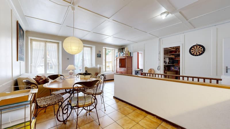 white walls, beige tiles, table with 4 chairs, round lamp, picture frame, radiator, dart board on wall