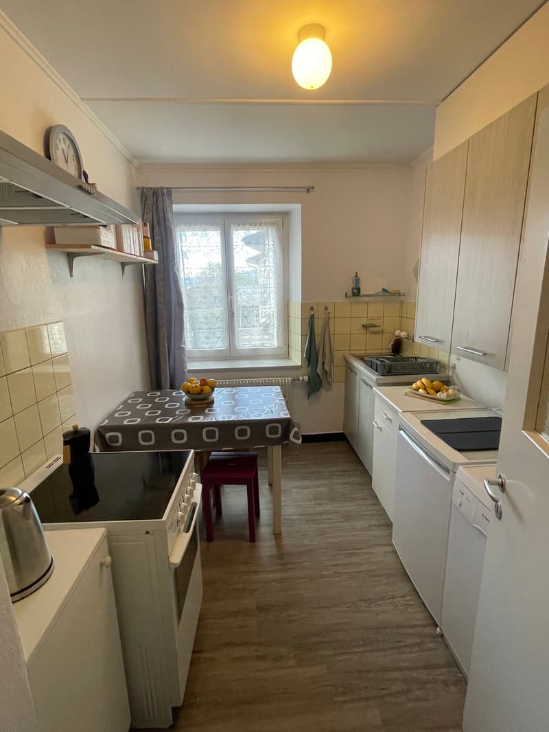 small kitchen, white cabinets, gas stove, oven, dishwasher, small dining table, light fixtures, clock on the wall, tiled flooring, small window, radiator