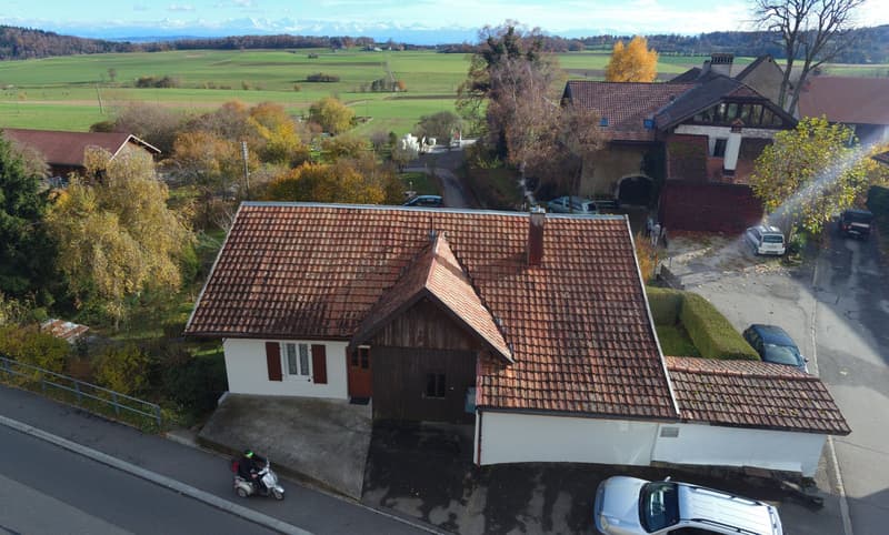 Detached house with tiled roof, wooden door, small attached garage, paved area in front