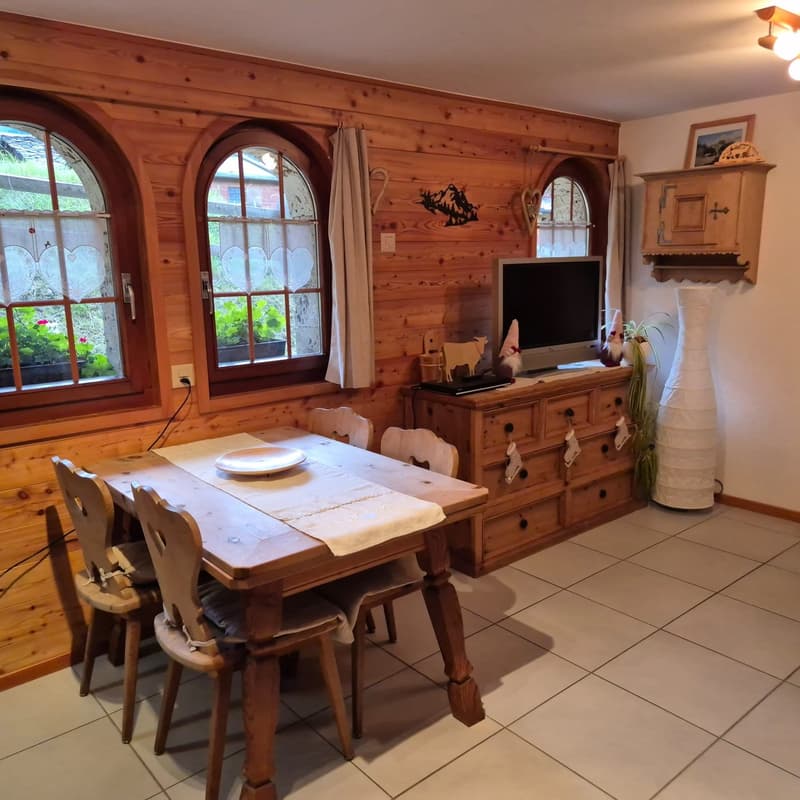 Dining room with wooden table, chairs, wooden cabinet, television on cabinet, plants, windows with curtains