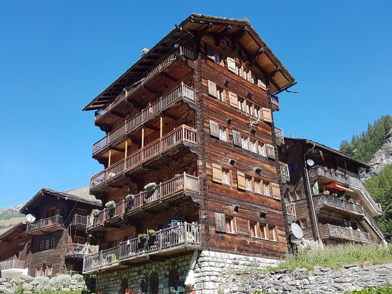 multi-story wooden building, multiple balconies, stone foundation, multiple windows, satellite dish