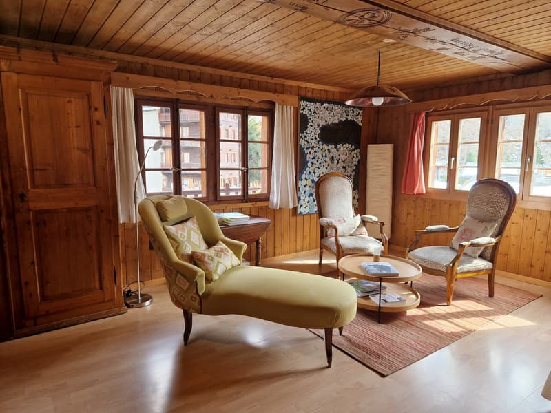 Wooden walls, wooden floor, 3 chairs, coffee table, rug, lamp, wooden cabinet, windows with curtains