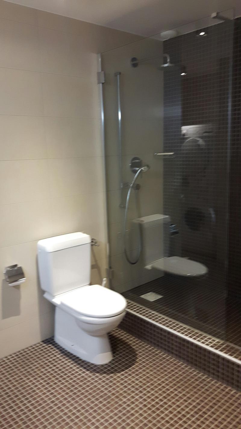 modern bathroom with white toilet, glass shower enclosure, tiled floor, and wall