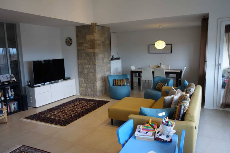 modern living room with a yellow sofa, blue chairs, a dining table, a TV, a rug, and a bookshelf