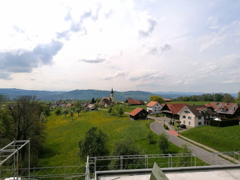 House in village with green hills, mountains, road, and cloudy sky