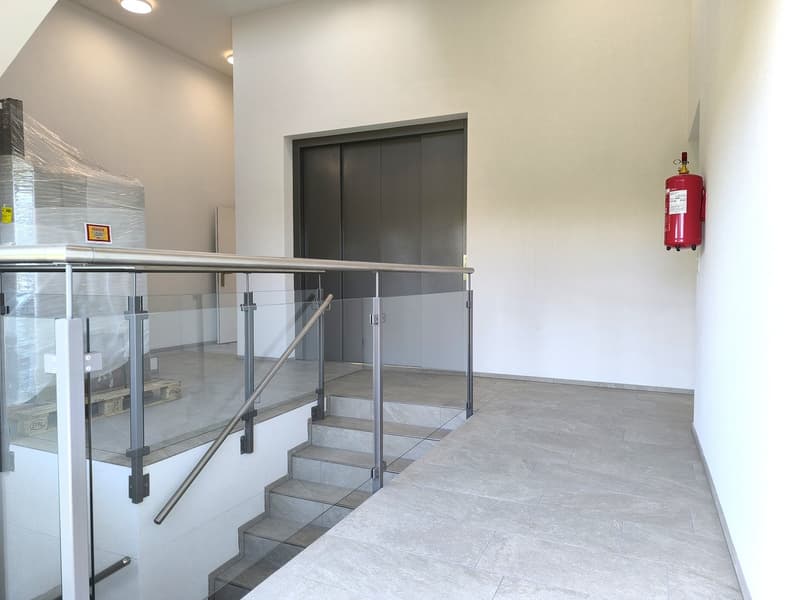 Tiled floor, stainless steel handrail, glass railing, grey elevator doors, fire extinguisher