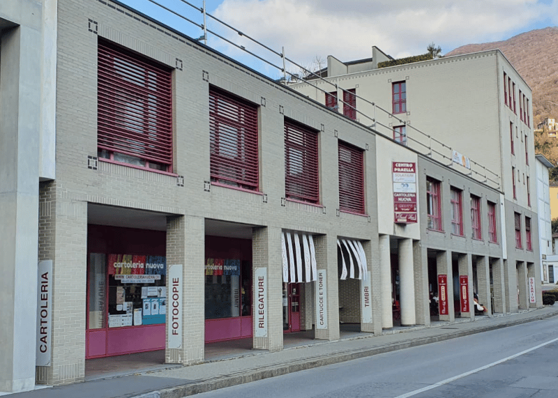 Two-story building, brick construction, red shutters, signage for various shops, multiple entrances