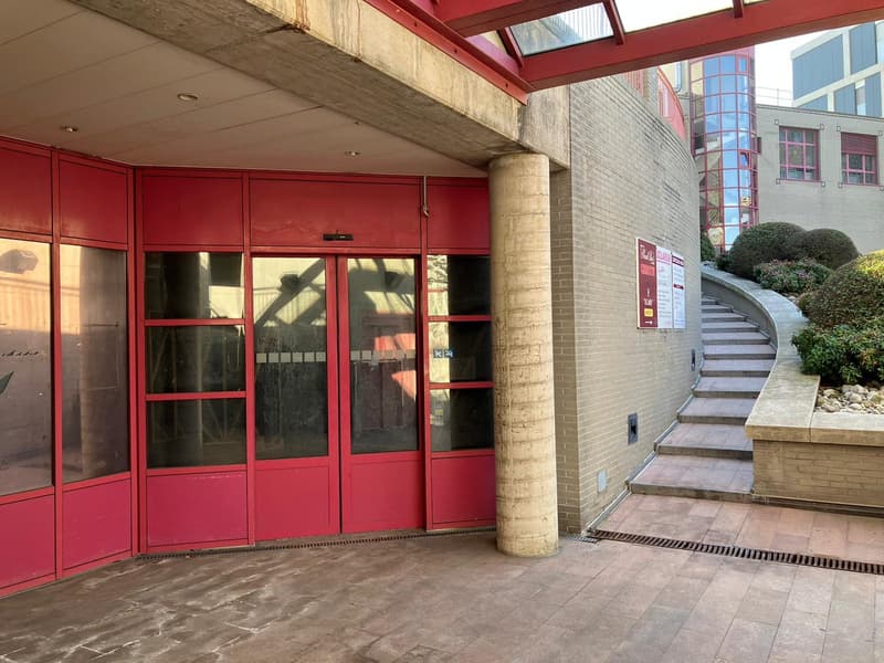 The building entrance with red doors, brick wall, staircase, and a covered roof.