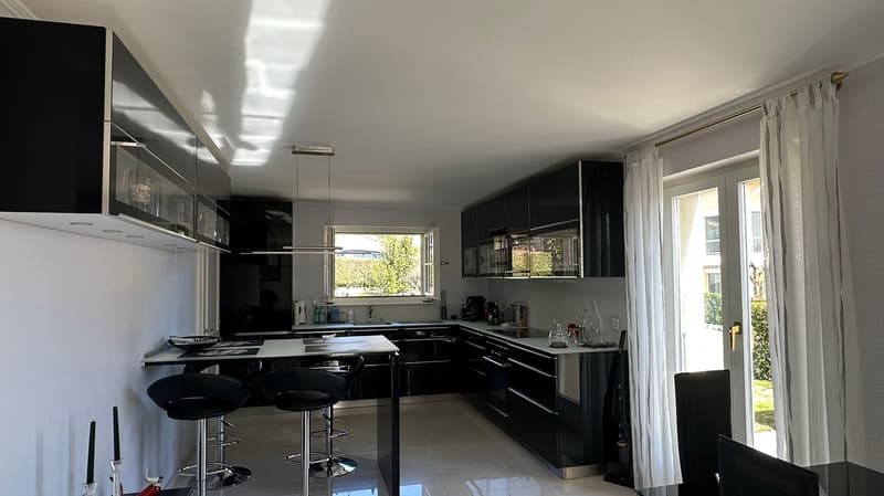 modern kitchen with black cabinets, white countertops, island with stools, large windows, white curtains, white tiled floor