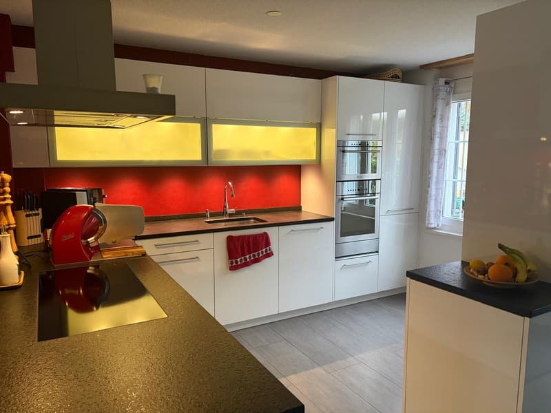 modern kitchen with white cabinets, red accent wall, granite countertops, stainless steel appliances, and a window with curtains