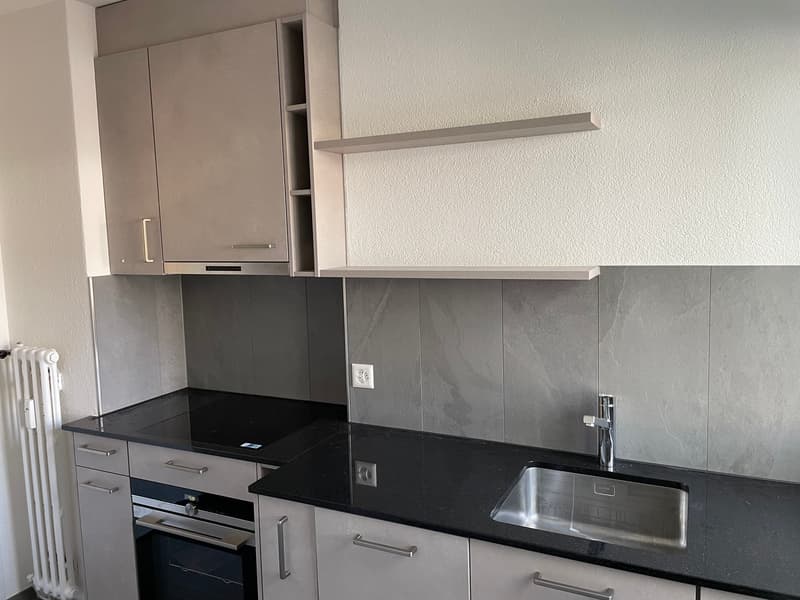 modern kitchen with black countertop, silver sink, gas stove, embedded oven, gray cabinets, open shelving, power outlet