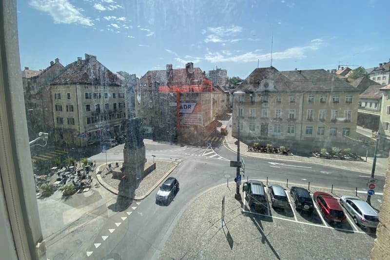 Aerial view of a building with multiple floors overlooking a roundabout, a parking area, and adjacent street with parked cars