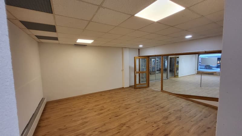 Office space with a wooden floor, white walls, glass entrance, open door to another room