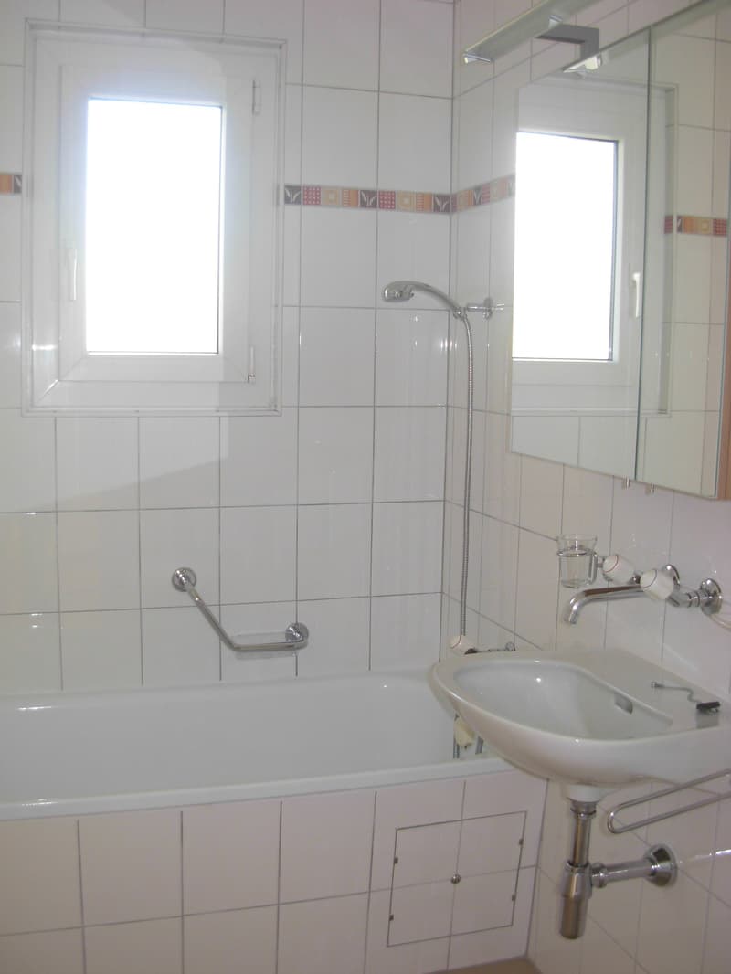Bathroom with white tiles, bathtub, sink, mirror, shower head, and faucet