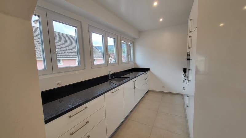 modern kitchen with white cabinets, black countertops, stainless steel sink, large windows, tiled floor