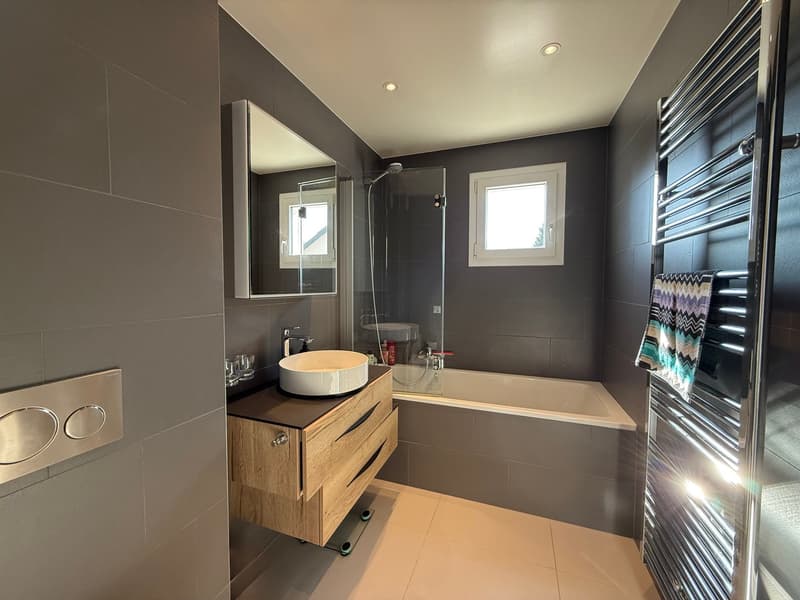 modern bathroom with gray tiles, white bathtub, wooden cabinet, round sink, glass shower enclosure, towel rack, mirror