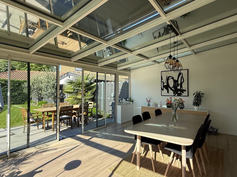 dining room with large glass walls, wooden floor, dining table, chairs, wooden ceiling, plants, artwork