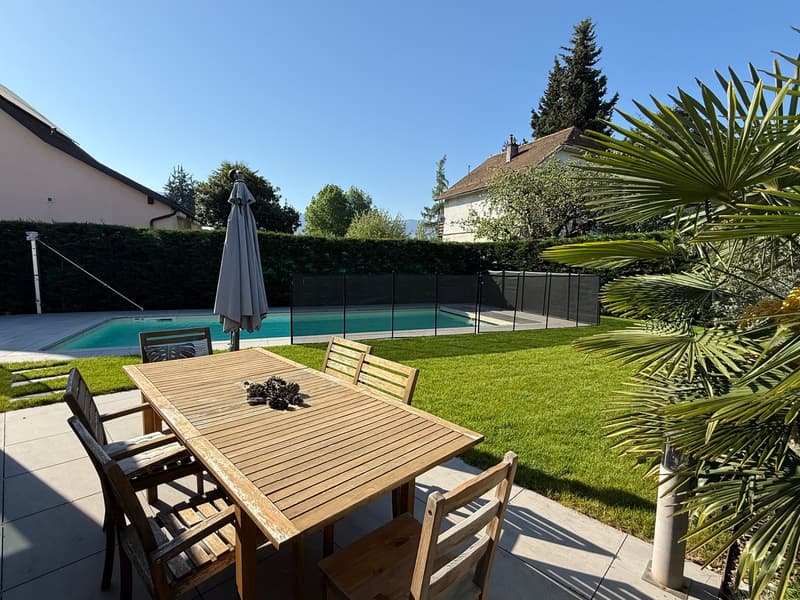 Wooden table and chairs, swimming pool, green lawn, trees, clear sky