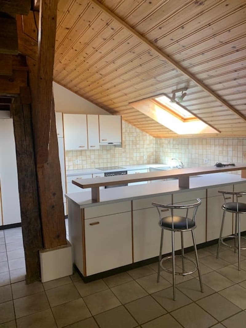 kitchen with white cabinetry, beige tiled floor, wooden beams, two barstools, and a kitchen island