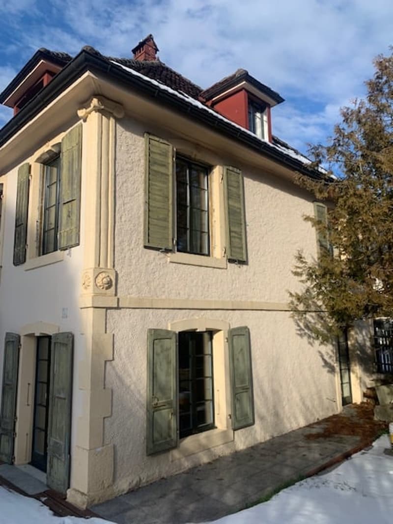 Two-story white house with red trim, dormer windows, green shutters, a tree in front, snow on the ground