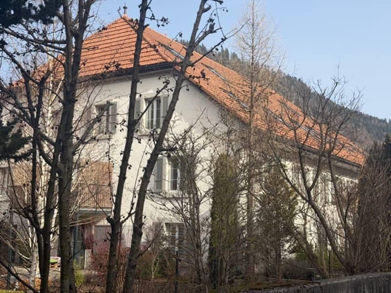 White house, red tiled roof, several windows, surrounded by trees, located on a hill