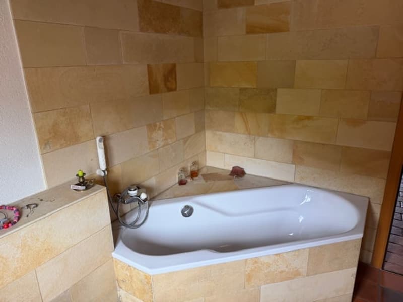 Bathroom with corner bathtub, beige tiles, shower head, faucet, and small shelf
