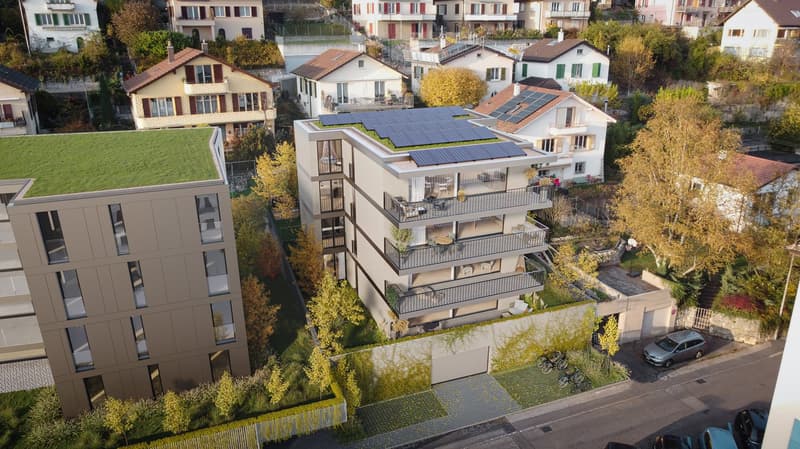 apartment building with several floors, solar panels on the roof, balconies on some floors, surrounding houses and greenery