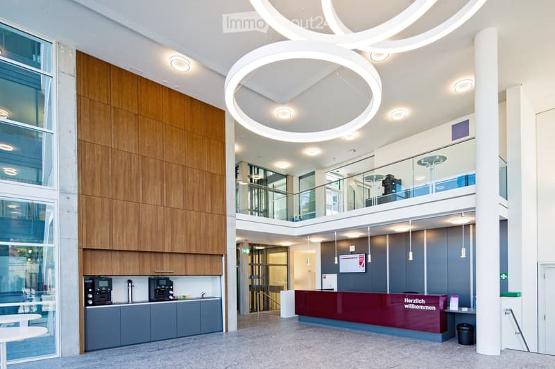 Spacious lobby with modern design, wood paneled walls, circular lighting fixtures, glass windows, reception desk, and kitchen appliances including a dishwasher