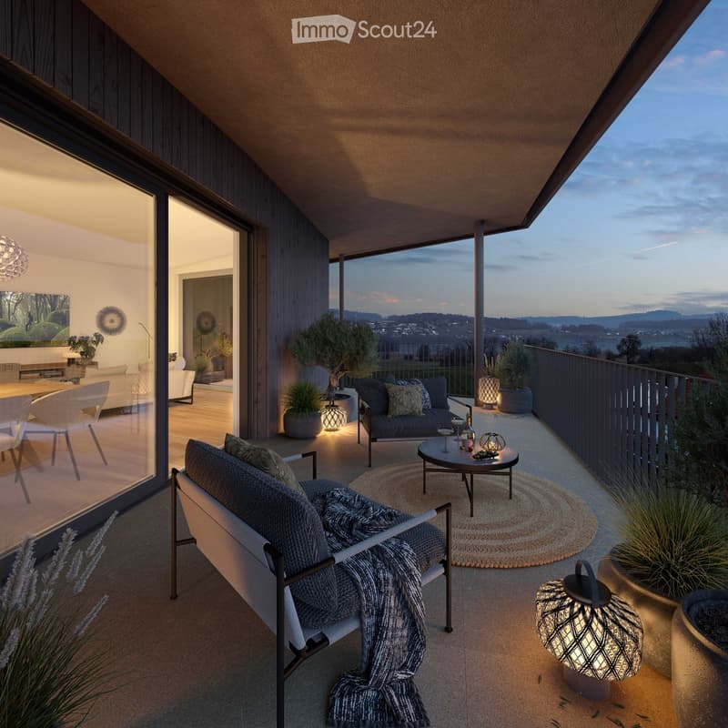 Outdoor terrace with wooden flooring, glass sliding doors, a couch with pillows, a table with decorative items, potted plants, a rug, and lamps, offering a view of a mountain and landscape