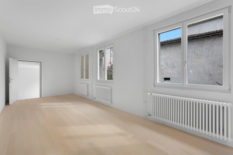 empty room with wooden floors, white walls, large windows with white frames, and radiators