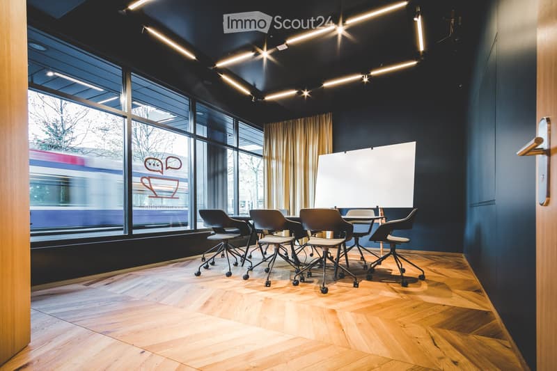 Meeting room with wooden floors, dark walls, large windows, movable chairs, whiteboard