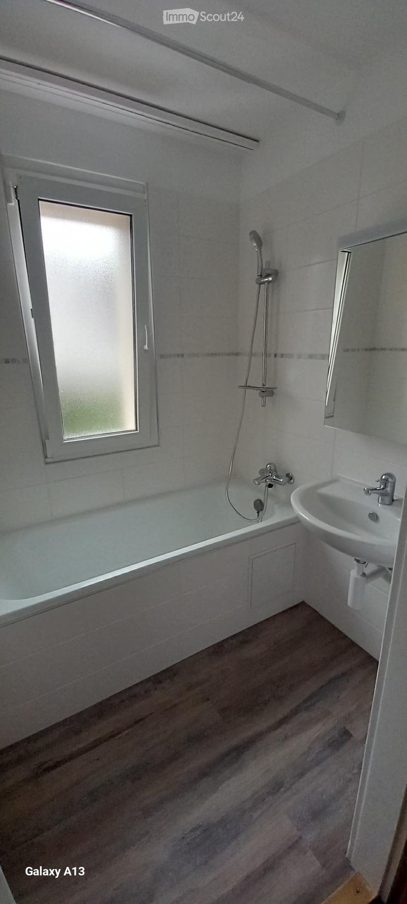 A bathtub, sink, shower, and mirror. Wooden flooring.