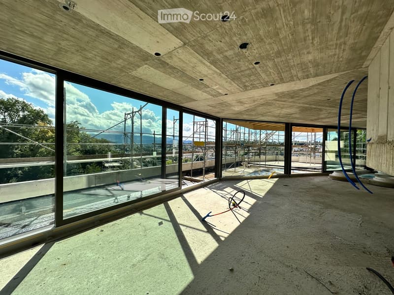 An unfinished room with large windows, concrete walls and floors, and scaffolding outside