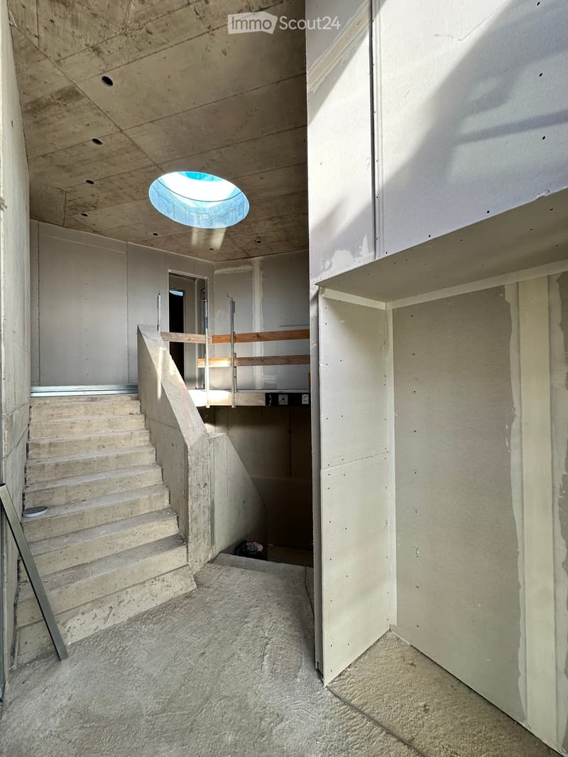 concrete staircase, landing with skylight, unfinished walls