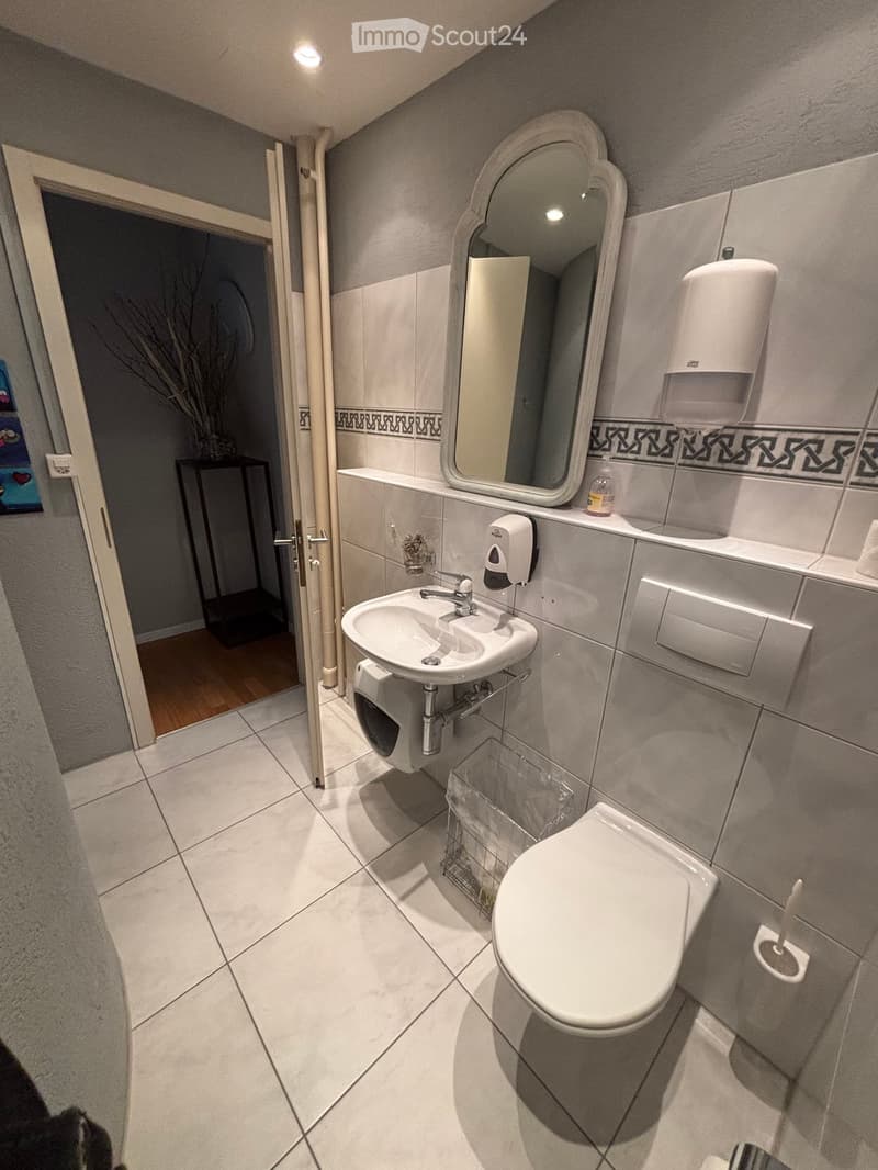 white tile flooring, white sink, white toilet, mirror, wall mounted soap dispenser, wall mounted tissue dispenser