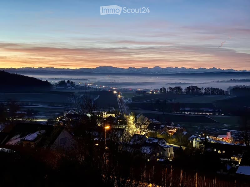 Wide aerial view of a town and landscape at dusk with mountains in the background