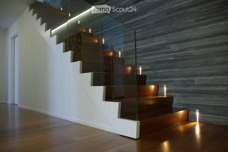 Modern staircase with glass panels, wooden steps, white walls, wooden floor, illuminated steps